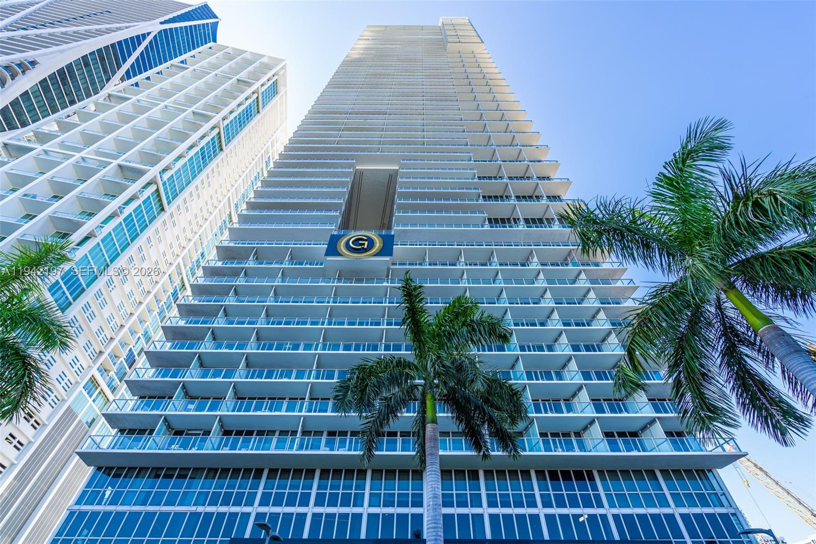 A low-angle view of a modern high-rise residential building with balconies and a logo — 1100 Biscayne Blvd # 2907, Miami FL 33132, MIAMI, FL