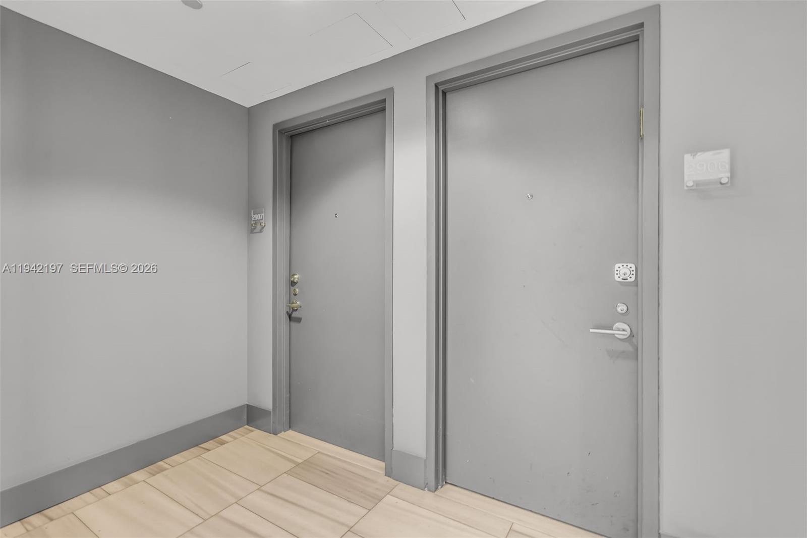 Two gray apartment doors are set in a hallway with light-colored tile flooring — 1100 Biscayne Blvd # 2907, Miami FL 33132, MIAMI, FL