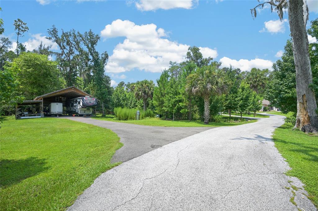 A paved driveway leads to a covered carport housing a recreational vehicle on a grassy lot — 19040 NW 88TH AVENUE ROAD, REDDICK, FL
