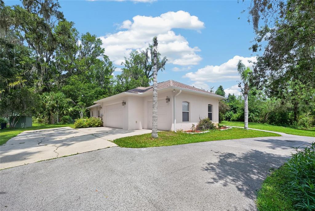 A light-colored detached garage with a concrete driveway sits on a grassy, tree-lined lot — 19040 NW 88TH AVENUE ROAD, REDDICK, FL