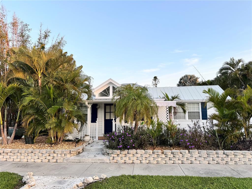 A white cottage with a metal roof and blue door sits behind a stone retaining wall — 701 BROADWAY STREET, LONGBOAT KEY, FL