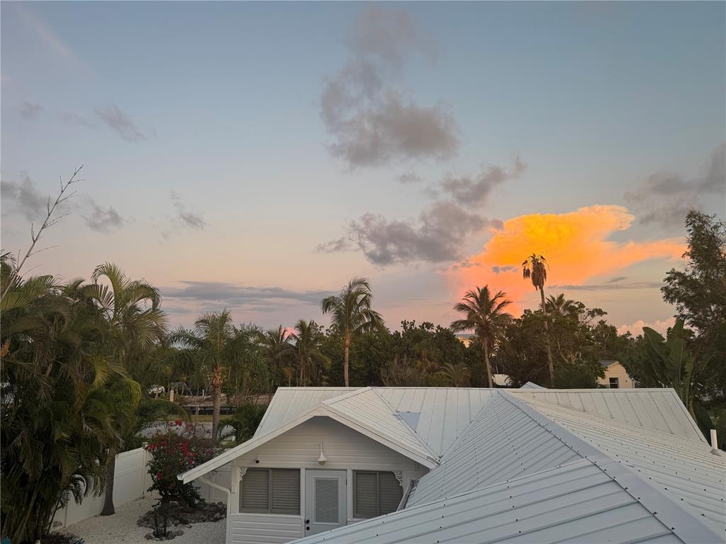 An elevated view of a white metal roof and palm trees against a sunset sky — 701 BROADWAY STREET, LONGBOAT KEY, FL