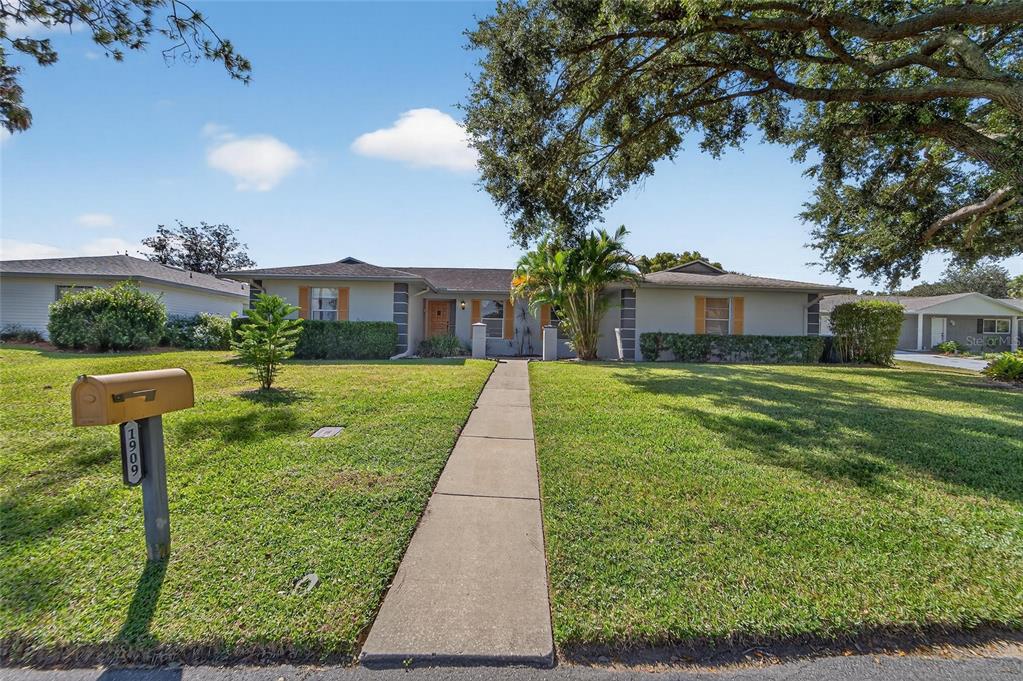 A single-story house with a gray exterior, a concrete walkway, and a large tree — 1909 KIMBALL COURT S, LAKELAND, FL
