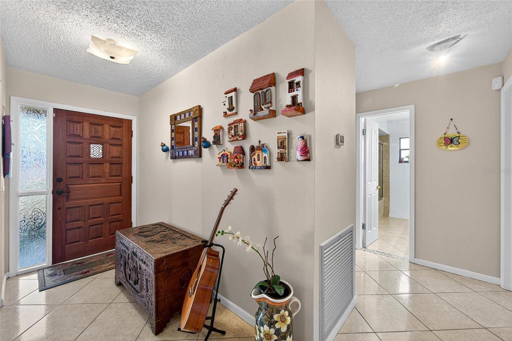 An entryway features a wooden door, a carved chest, a guitar, and wall-mounted decorative houses — 1909 KIMBALL COURT S, LAKELAND, FL