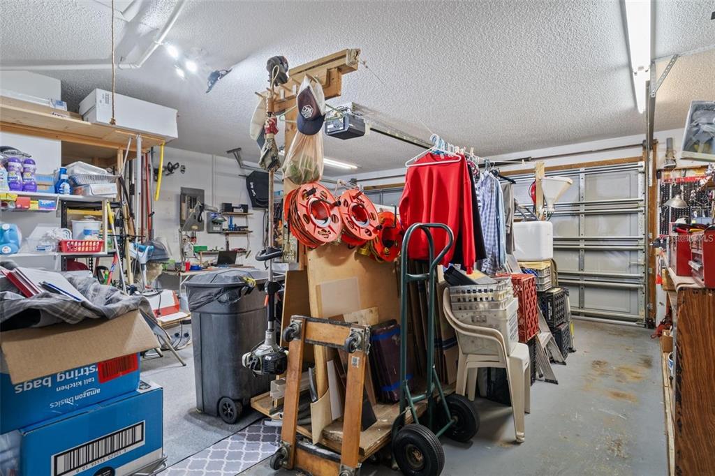 A cluttered garage features a central wooden storage cart, hanging clothes, and various household items — 8914 SCHRADER BOULEVARD, PORT RICHEY, FL