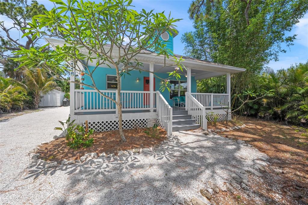A bright blue cottage features a white wrap-around porch, lattice skirting, and a gravel driveway — 116 AVENIDA LA PALMA, NOKOMIS, FL