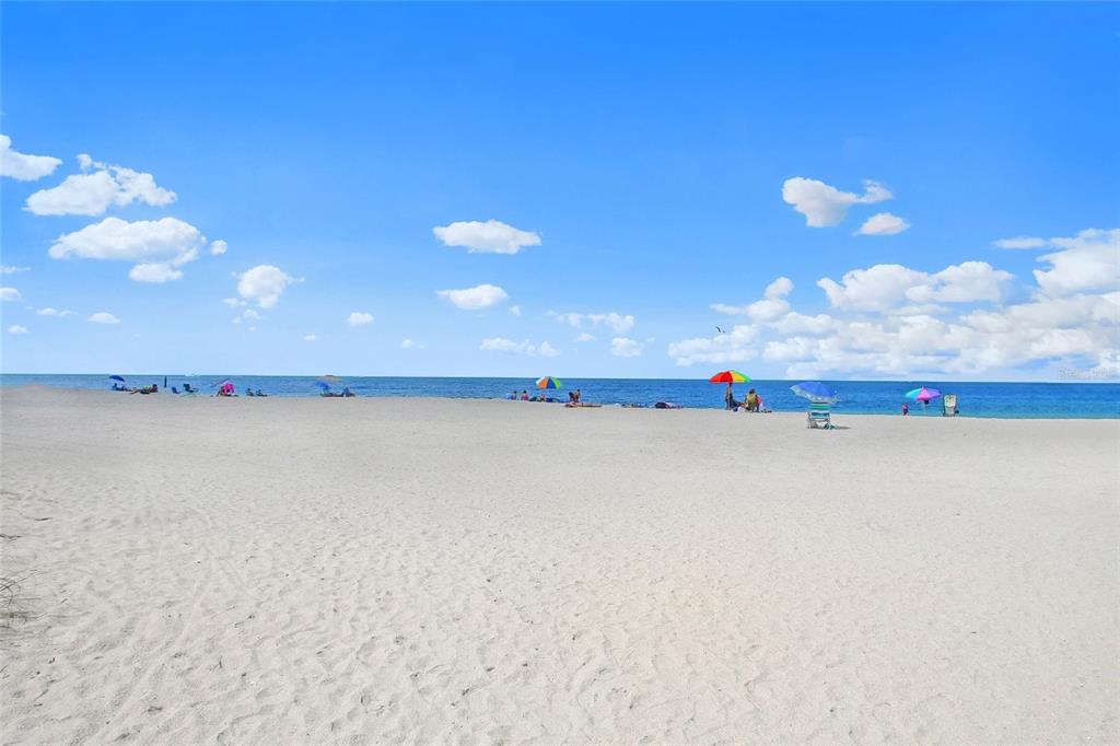 A wide, sandy beach stretches toward the ocean under a bright blue sky with clouds — 116 AVENIDA LA PALMA, NOKOMIS, FL