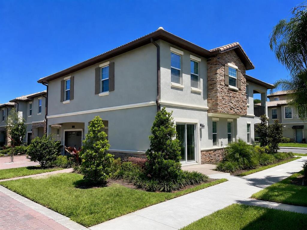 A two-story townhouse exterior with light gray stucco, stone accents, and a tiled roof — 1312 SHINNECOCK HILLS DRIVE UNIT 1312, DAVENPORT, FL
