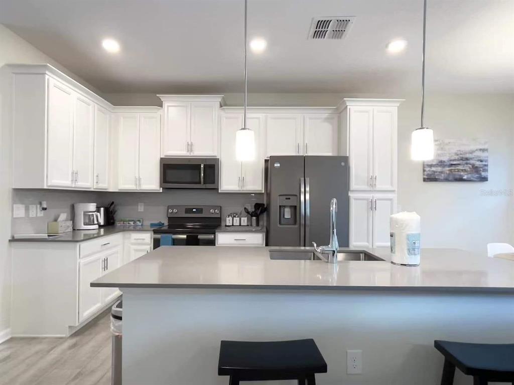 A modern kitchen features white cabinets, gray countertops, stainless steel appliances, and a central island — 1312 SHINNECOCK HILLS DRIVE UNIT 1312, DAVENPORT, FL