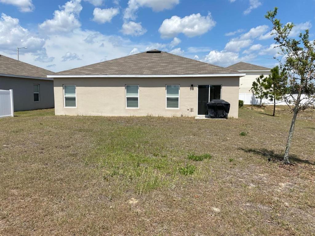 The rear exterior of a single-story house features a tan stucco facade and sliding glass doors — 372 ROOKS LOOP, HAINES CITY, FL