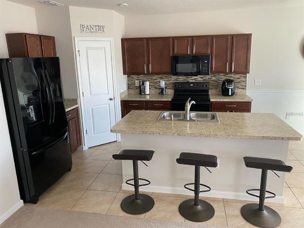 A kitchen features dark wood cabinets, a granite island with three stools, and black appliances — 372 ROOKS LOOP, HAINES CITY, FL