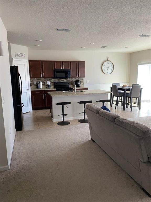 An open-concept kitchen features dark wood cabinets, a central island with bar seating, and appliances — 372 ROOKS LOOP, HAINES CITY, FL
