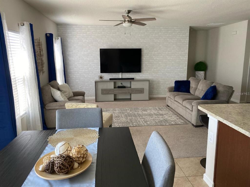 A living room with a brick-patterned accent wall, a television, and a dining area — 372 ROOKS LOOP, HAINES CITY, FL