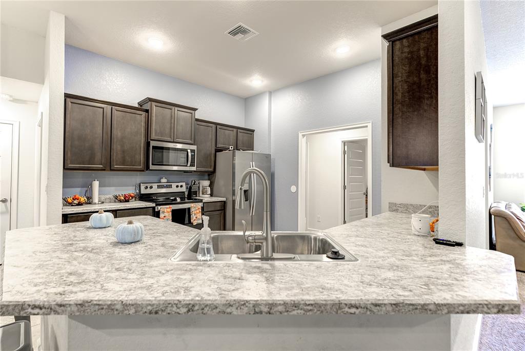 A kitchen features dark wood cabinets, a stainless steel refrigerator, and a granite-patterned island countertop — 71 BELLS OF IRELAND COURT, HOMOSASSA, FL