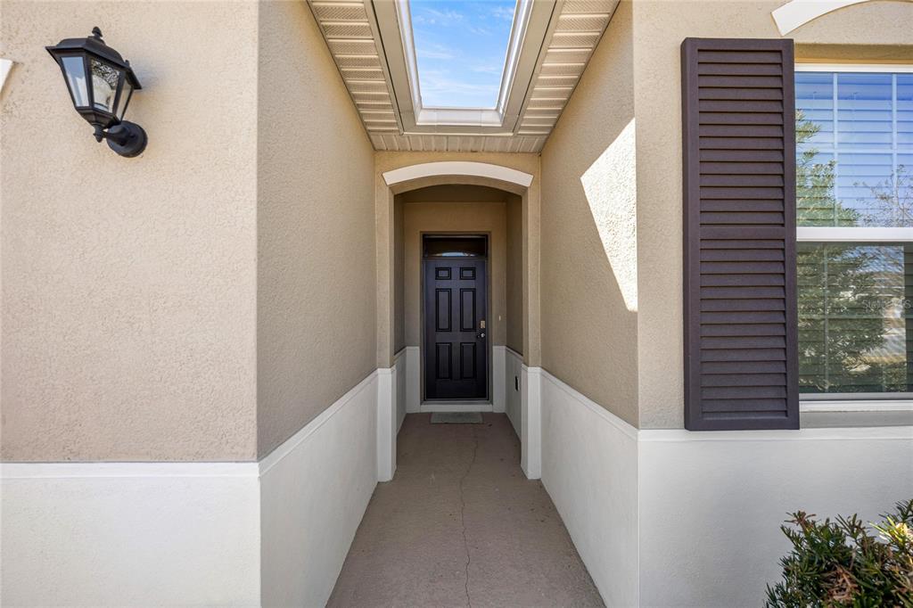 A recessed entryway features a dark front door, a skylight, and a beige stucco exterior — 4336 NW 55TH COURT, OCALA, FL