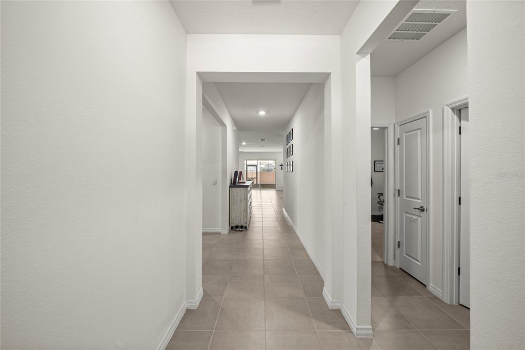 A tiled hallway leads past two closed doors toward a bright, open living area — 4336 NW 55TH COURT, OCALA, FL