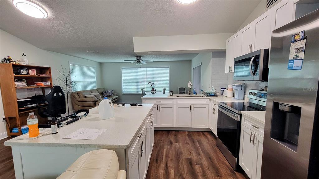 A kitchen with white cabinets and a large island opens into a living area — 7051 WENTWORTH WAY, NEW PORT RICHEY, FL