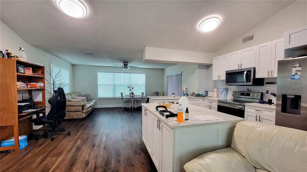 An open-concept kitchen and living area features white cabinetry, a central island, and wood flooring — 7051 WENTWORTH WAY, NEW PORT RICHEY, FL