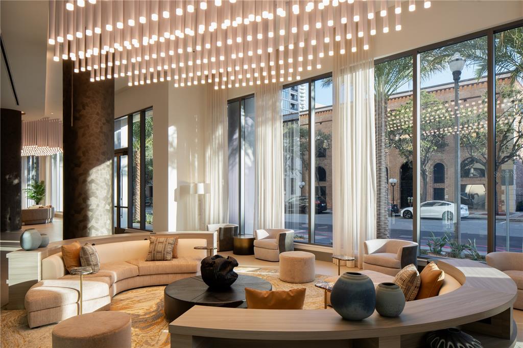 A modern lobby features a curved sofa, a large chandelier, and floor-to-ceiling windows — 275 1ST AVENUE S UNIT 3205, ST PETERSBURG, FL