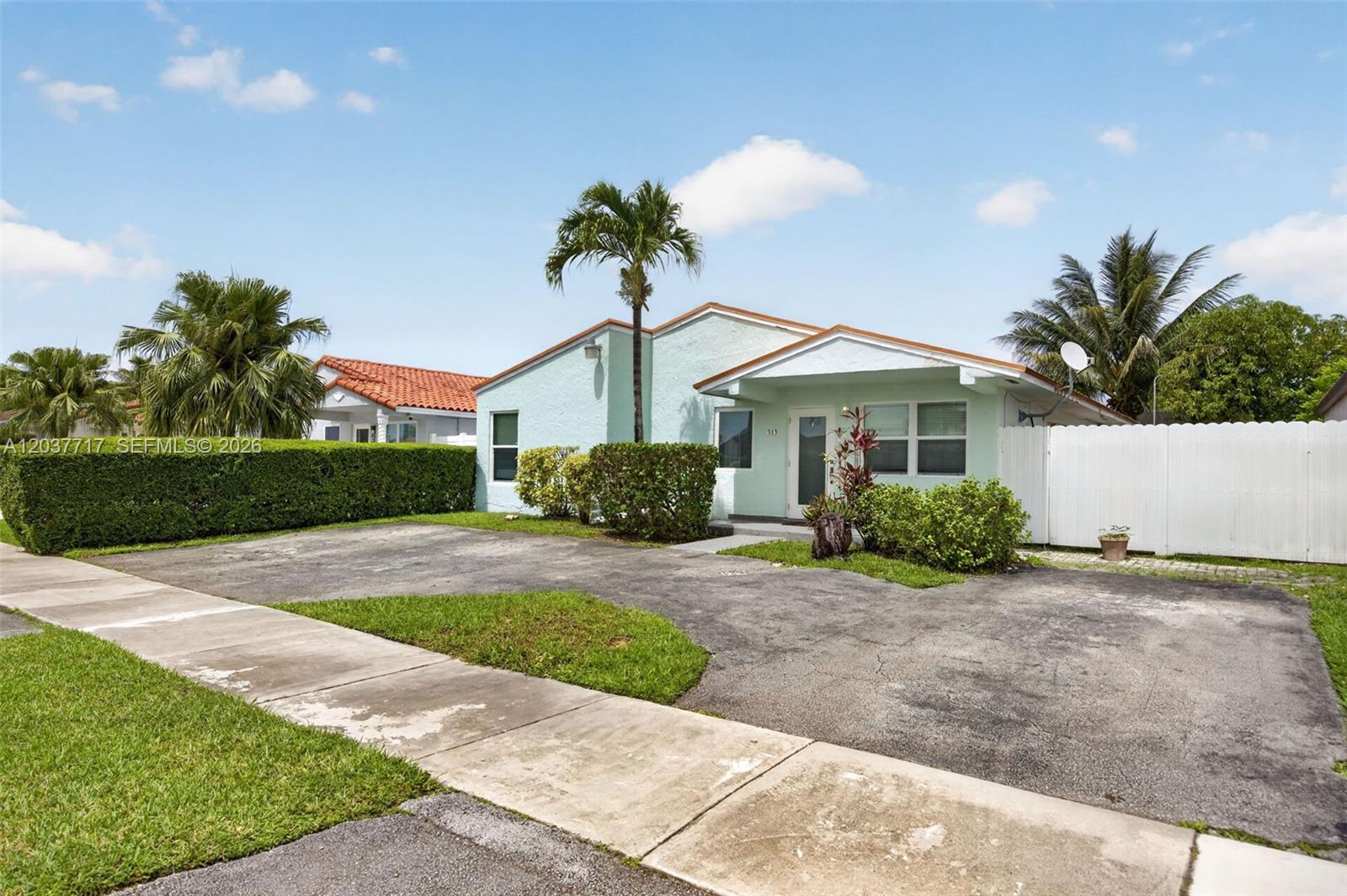 A light green single-story house features a paved driveway and a white privacy fence — 313 NW 132nd Pl, Miami FL 33182, MIAMI, FL