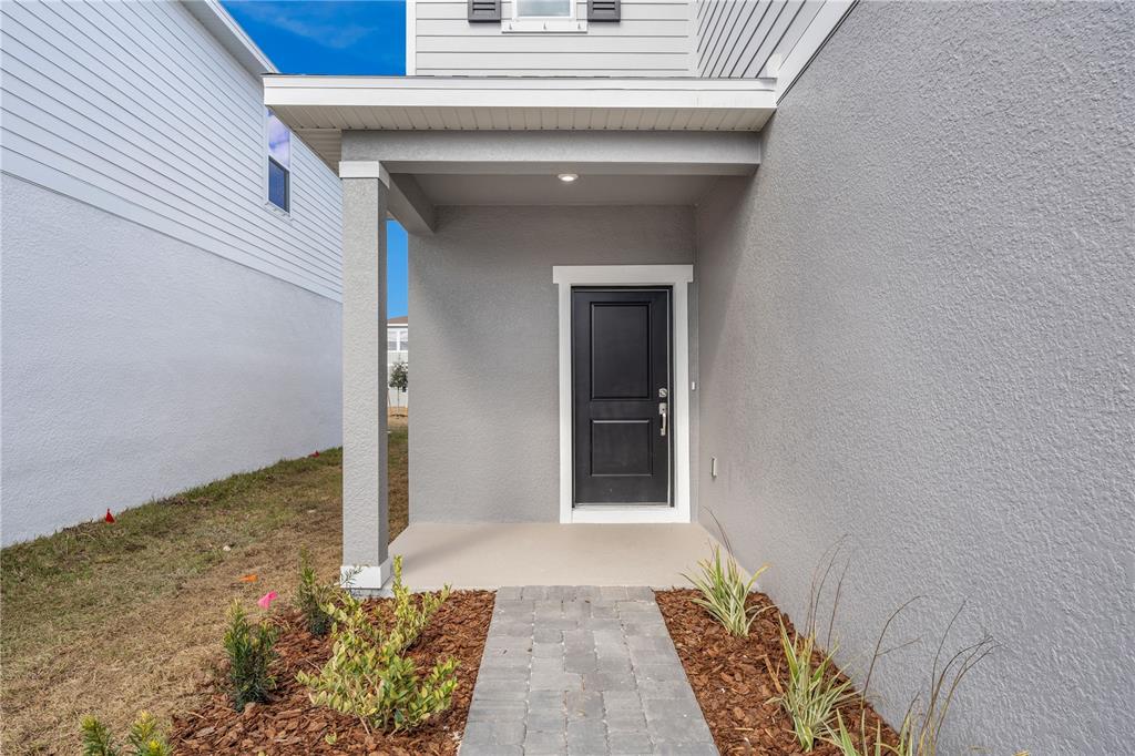 A gray house exterior features a covered entryway with a black door and stone walkway — 10104 MORNING MEADOWLARK TRAIL, PARRISH, FL