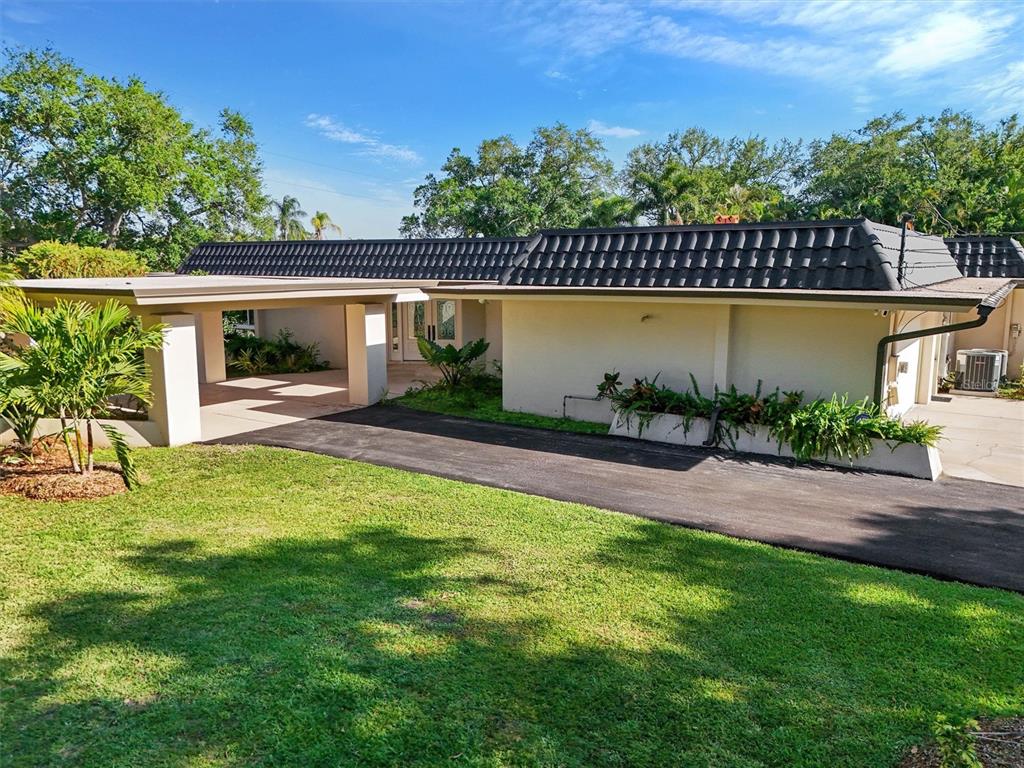 A single-story house with a dark tiled roof, a carport, and a paved driveway — 1875 BELLEAIR ROAD, CLEARWATER, FL