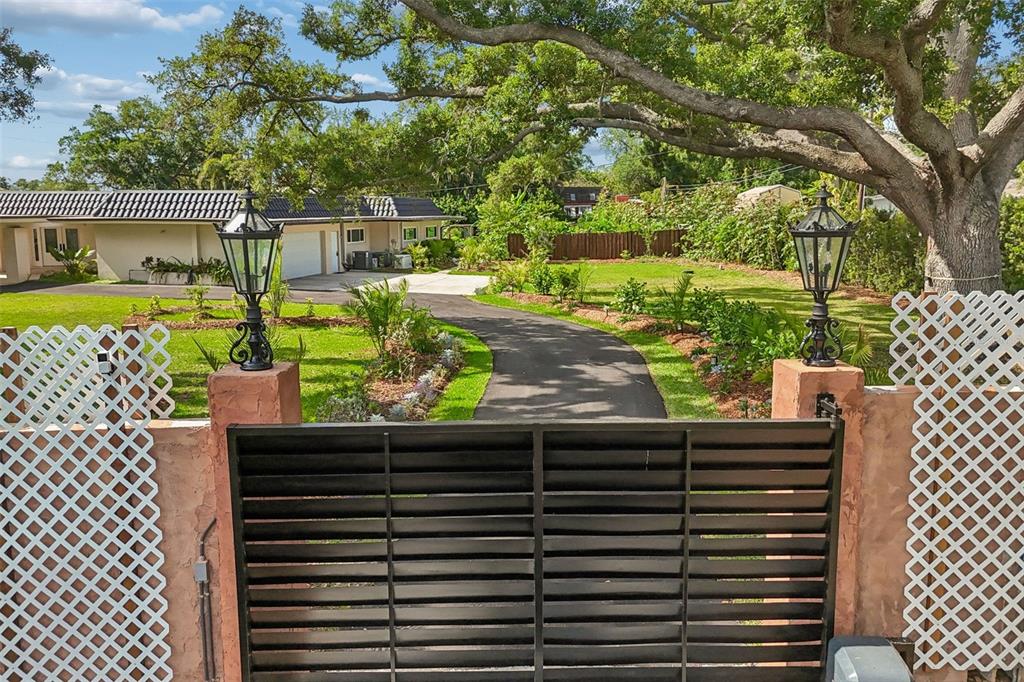 A black metal gate with lattice side panels opens to a driveway leading to a house — 1875 BELLEAIR ROAD, CLEARWATER, FL
