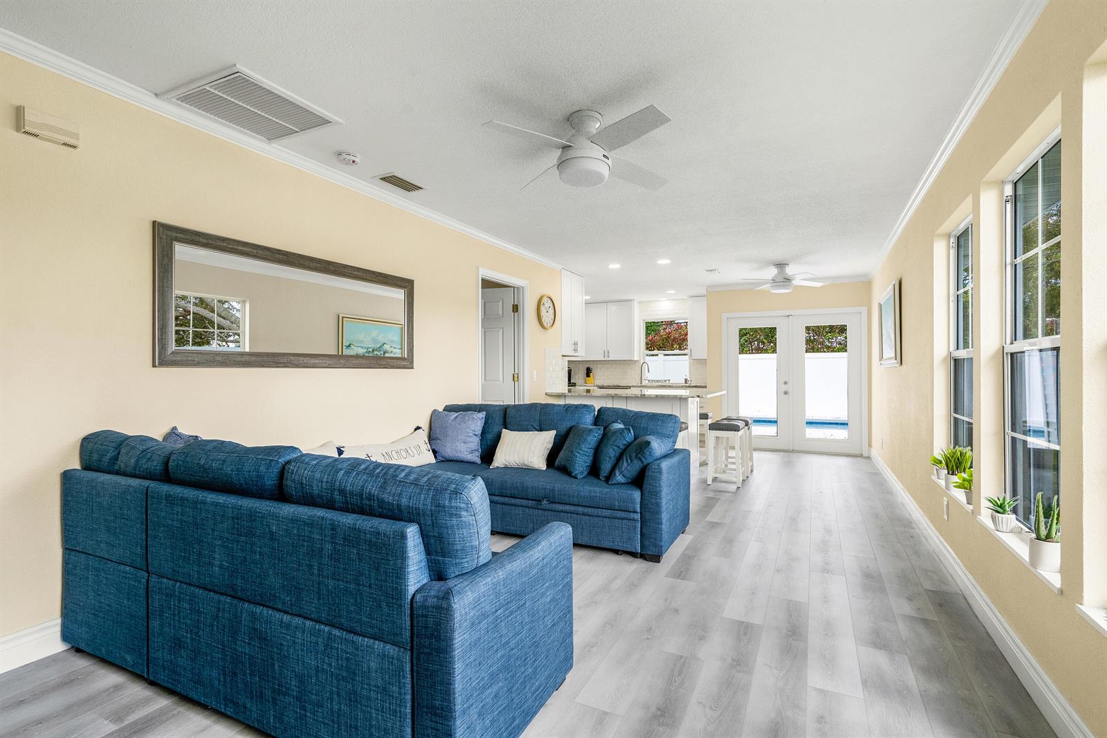 A living room with a blue sectional sofa, light wood-look flooring, and an open kitchen — 1510 3rd Court, Vero Beach FL 32960, VERO BEACH, FL
