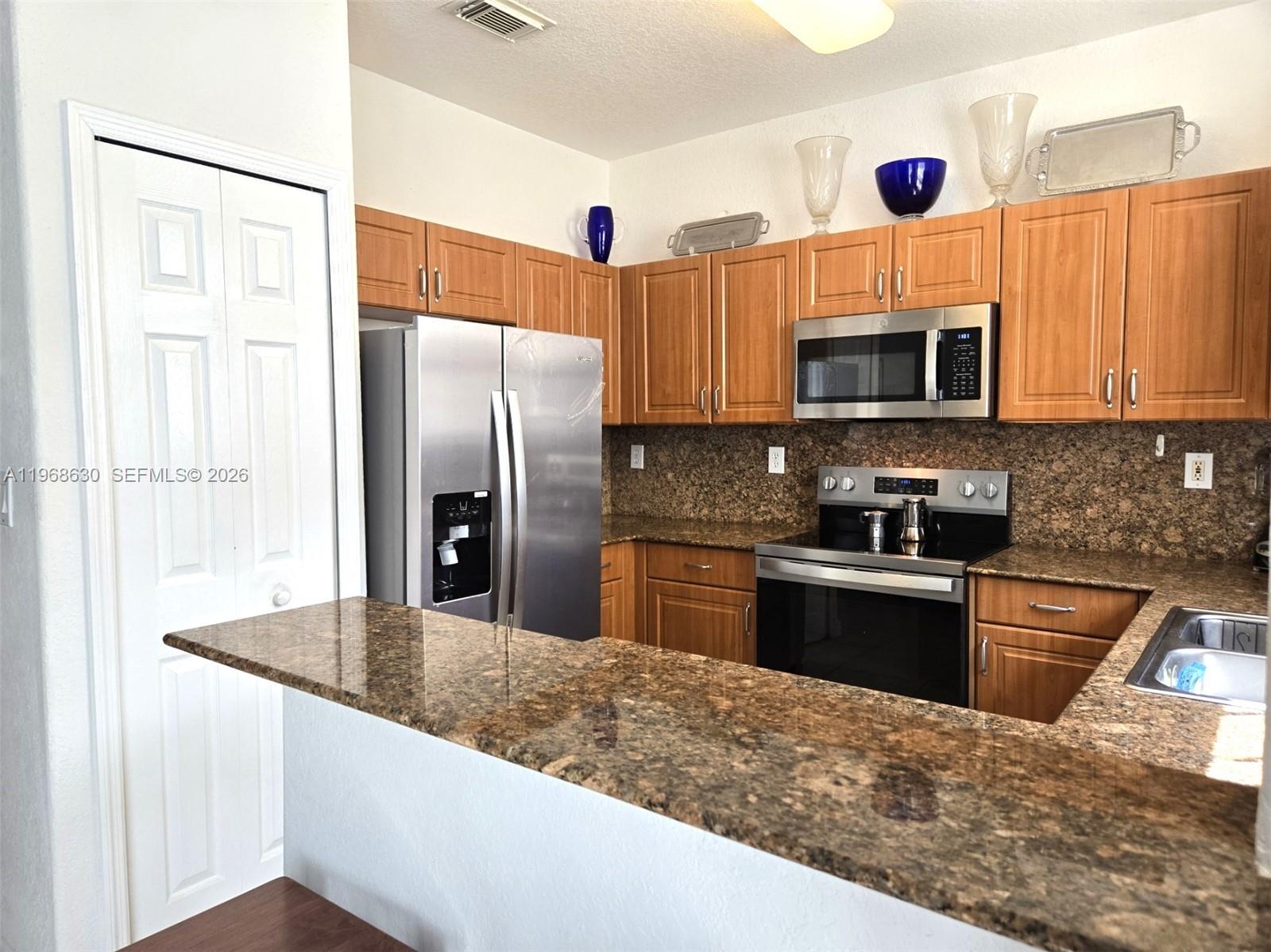A kitchen features wood cabinets, granite countertops, stainless steel appliances, and a breakfast bar — 10840 NW 79th St, Doral FL 33178, DORAL, FL