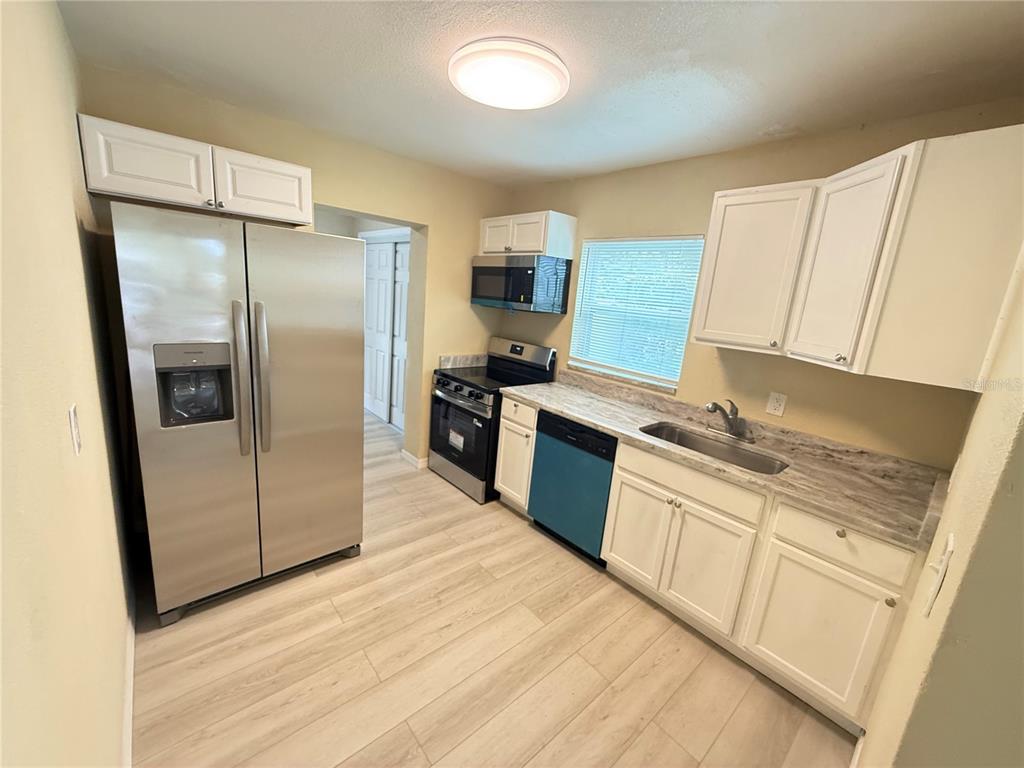 A kitchen featuring white cabinets, stainless steel appliances, a blue dishwasher, and light wood flooring — 13917 3RD STREET, DADE CITY, FL