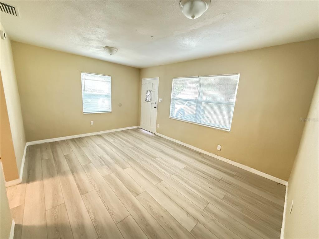 An empty room features light wood-look flooring, beige walls, two windows with blinds, and a door — 13917 3RD STREET, DADE CITY, FL
