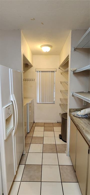 A narrow laundry room features a white refrigerator, stacked washer-dryer, open shelving, and tiled floors — 3404 NW 52ND TERRACE, GAINESVILLE, FL