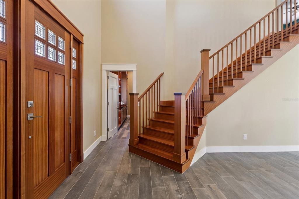 An entryway with wood-paneled doors, a wooden staircase, and gray wood-look tile flooring — 15503 TROTTING HORSE LANE, TAVARES, FL