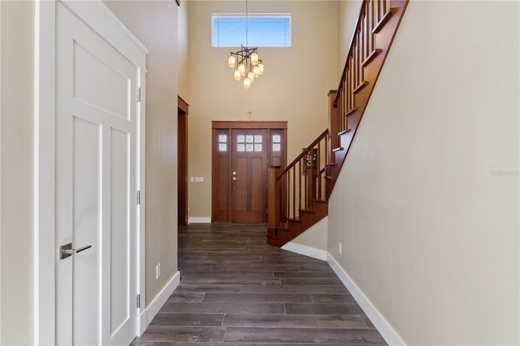 A high-ceilinged foyer features wood-look tile flooring, a wooden staircase, and a front door — 15503 TROTTING HORSE LANE, TAVARES, FL