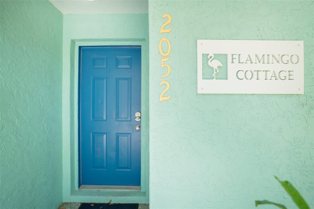 A blue front door is set into a light green wall with a cottage sign — 2051 ROSELAWN STREET, SARASOTA, FL
