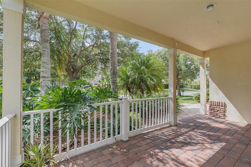 A covered porch with brick pavers, a white railing, and views of trees and landscaping — 13406 BUDWORTH CIRCLE, ORLANDO, FL