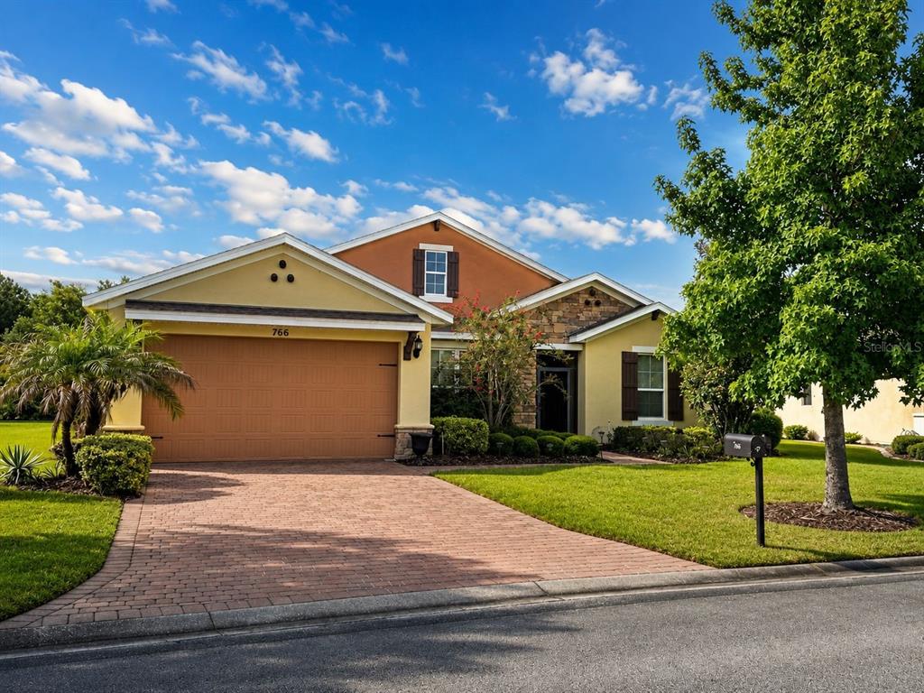A single-story house with a tan stucco exterior, stone accents, and a brick paver driveway — 766 CARMEL LANE, KISSIMMEE, FL