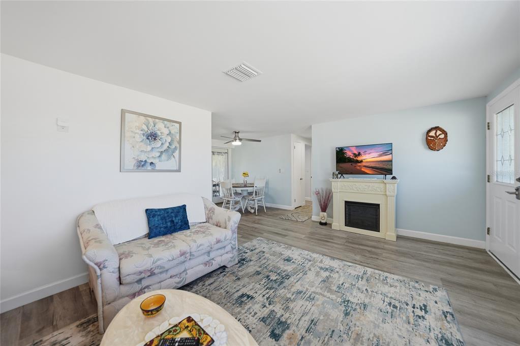 A living room features a floral sofa, a fireplace with a television, and wood-look flooring — 19909 MIDWAY BOULEVARD, PORT CHARLOTTE, FL