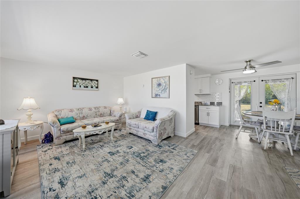 A living room and dining area feature light wood-look flooring, white walls, and floral furniture — 19909 MIDWAY BOULEVARD, PORT CHARLOTTE, FL