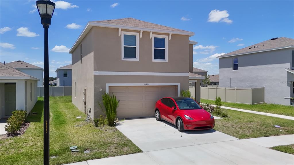 A two-story tan house with a two-car garage and a red car parked outside — 33327 DARLEY DALE TRAIL, WESLEY CHAPEL, FL