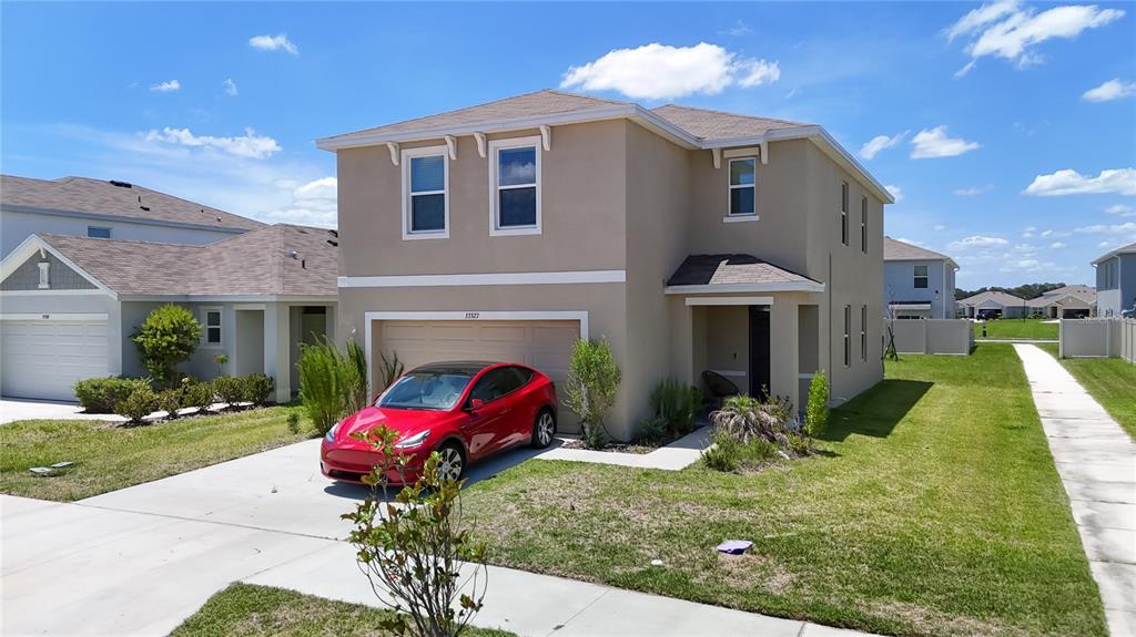 A two-story tan house with a red car parked in the driveway under a blue sky — 33327 DARLEY DALE TRAIL, WESLEY CHAPEL, FL