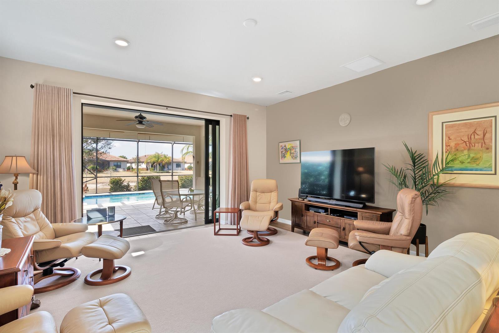 A living room with leather recliners, a television, and a sliding door opening to a pool — 5021 Monroe Circle, Vero Beach FL 32967, VERO BEACH, FL