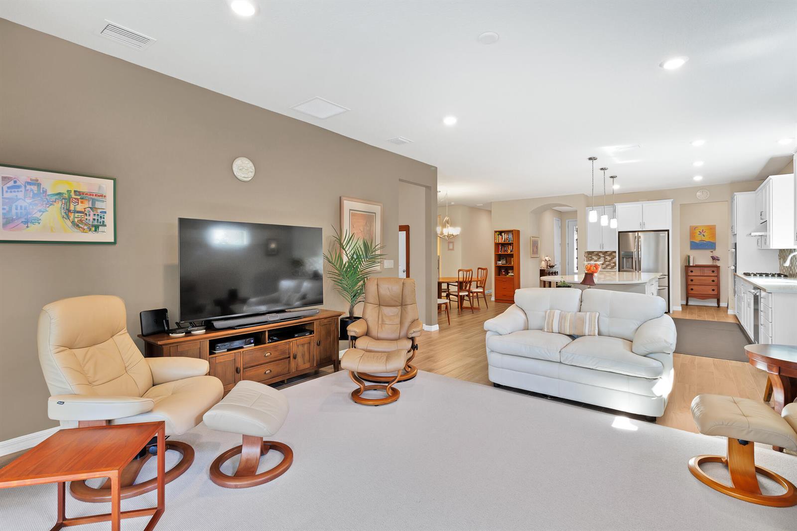 An open-concept living room features a television, leather recliners, a white sofa, and a kitchen — 5021 Monroe Circle, Vero Beach FL 32967, VERO BEACH, FL
