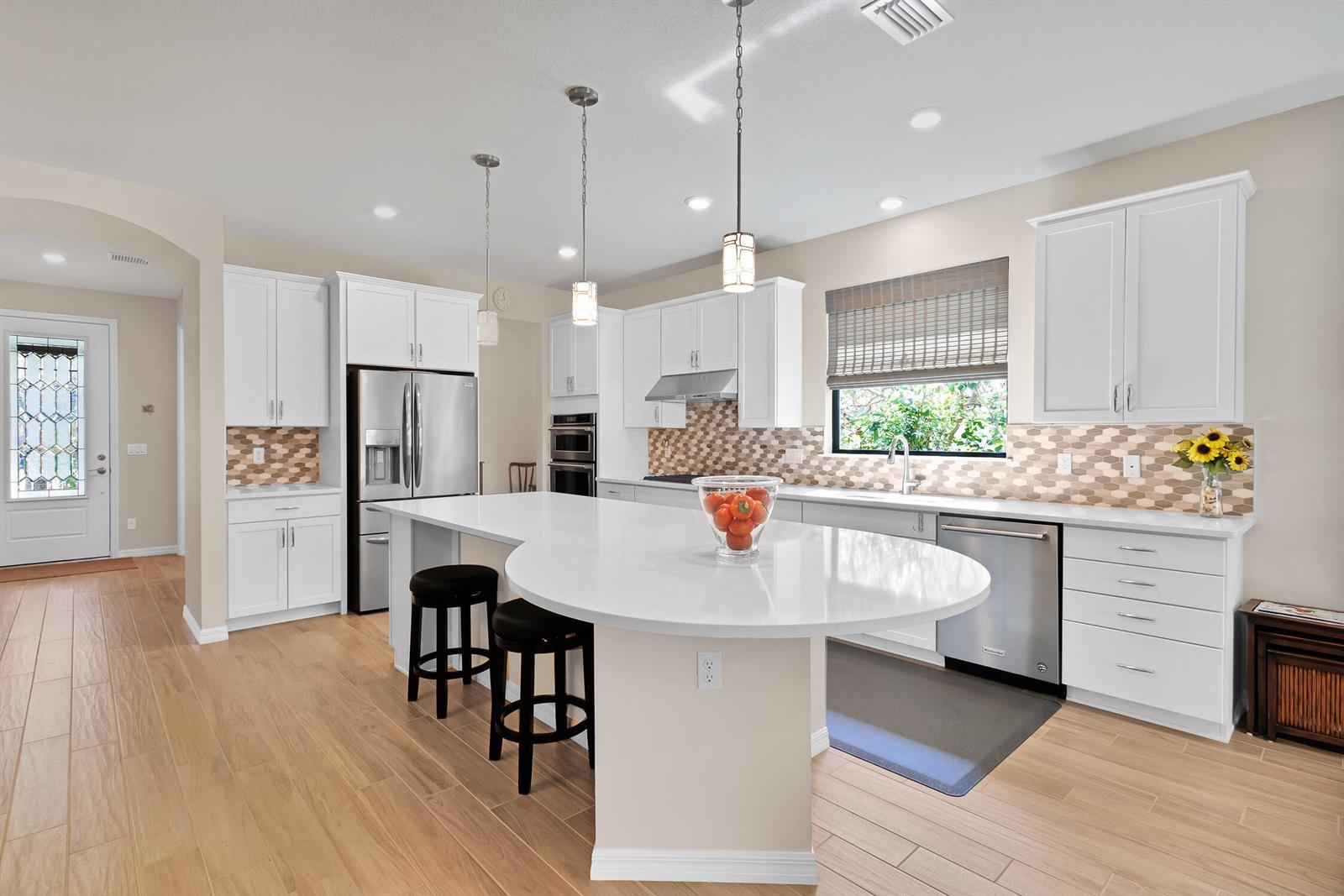 A modern kitchen features white cabinetry, a large curved island, and light wood-look flooring — 5021 Monroe Circle, Vero Beach FL 32967, VERO BEACH, FL