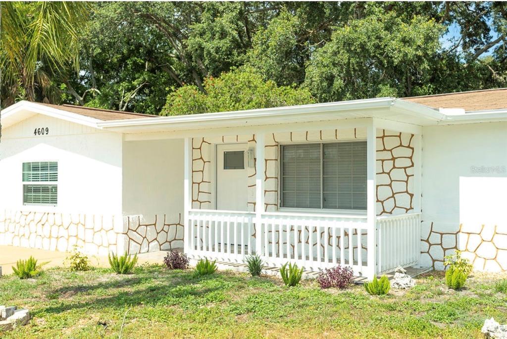 A white house exterior features a covered front porch, stone-patterned wainscoting, and a front lawn — 4609 IRENE LOOP, NEW PORT RICHEY, FL