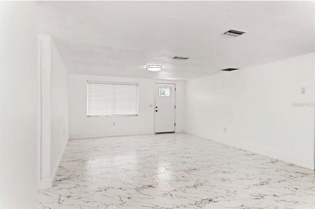 An empty room with white walls, a white door, and white marble-patterned tile flooring — 4609 IRENE LOOP, NEW PORT RICHEY, FL