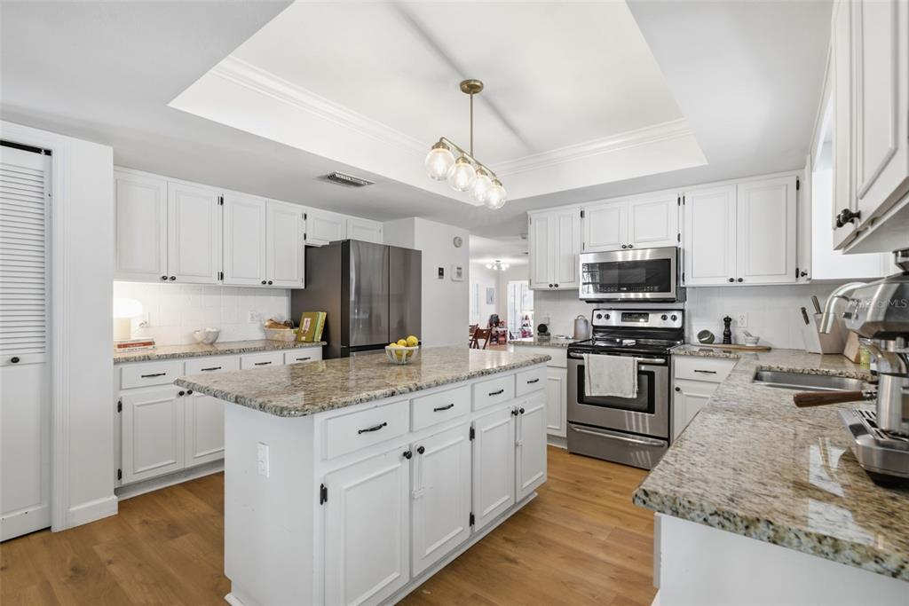 A kitchen features white cabinetry, granite countertops, a central island, and stainless steel appliances — 16909 ROLLING ROCK DRIVE, TAMPA, FL