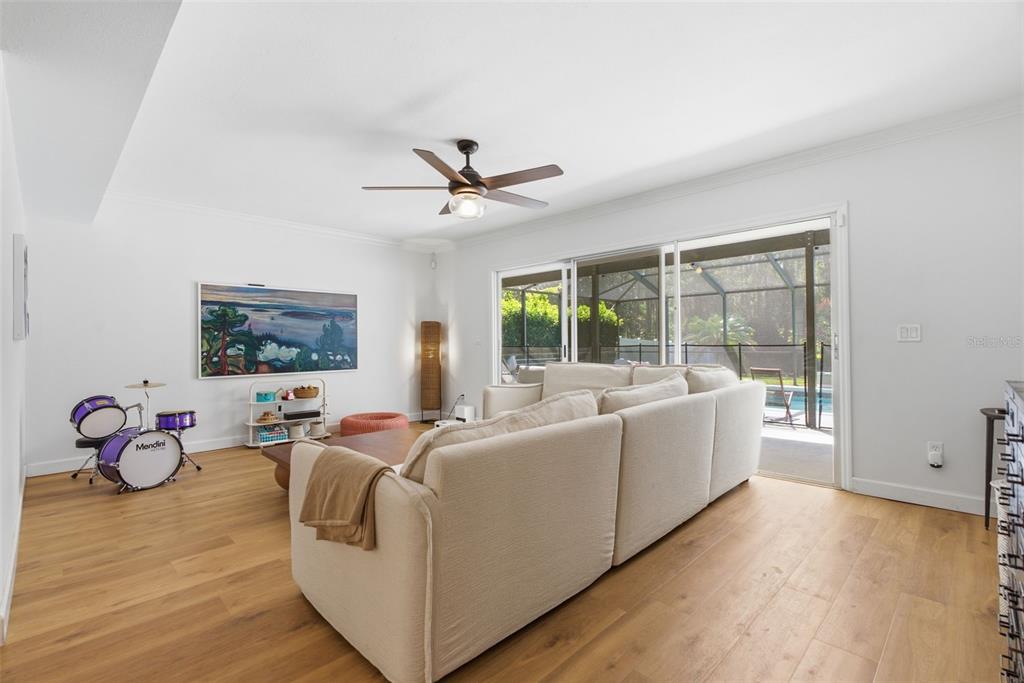 A living room features light wood flooring, a large beige sectional, and a purple drum set — 16909 ROLLING ROCK DRIVE, TAMPA, FL