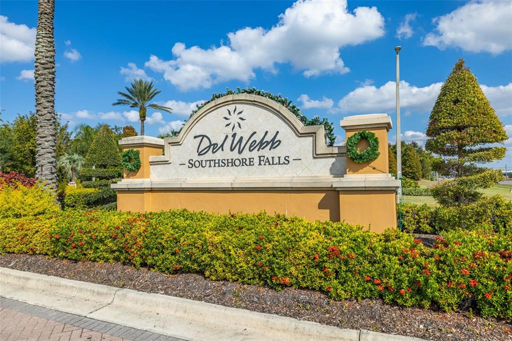 A beige monument sign for Del Webb Southshore Falls stands amidst landscaping and palm trees — 5808 HIDDEN FALLS LANE, APOLLO BEACH, FL