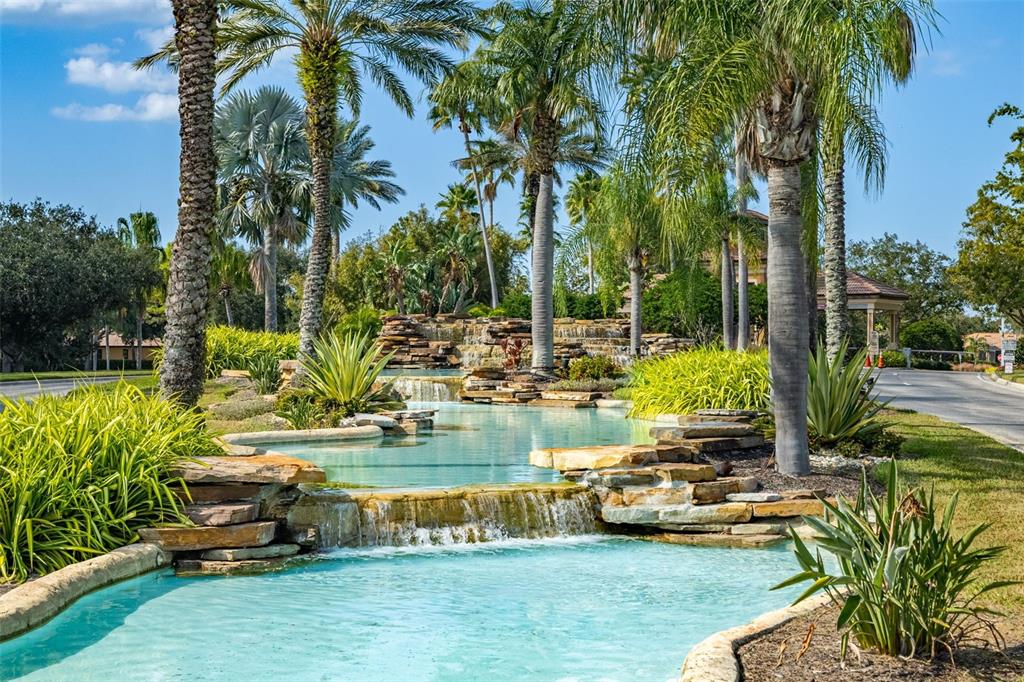 A tiered stone waterfall flows into a turquoise pool surrounded by palm trees and landscaping — 5808 HIDDEN FALLS LANE, APOLLO BEACH, FL